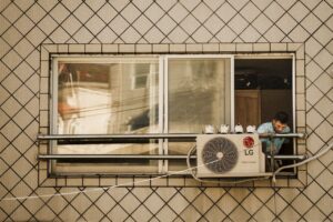 Man looks outside a window with an LG air conditioner unit visible, creating a reflective effect.