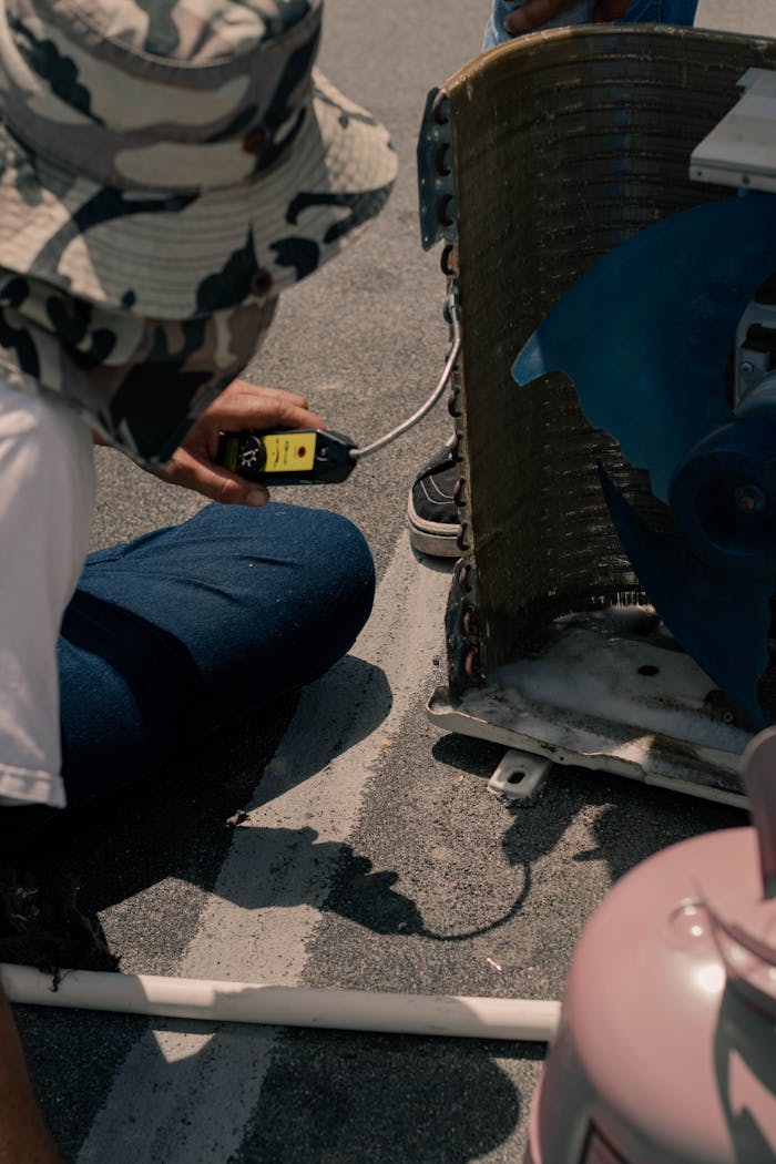 A technician tests an air conditioning unit with a multimeter outdoors on a sunny day.